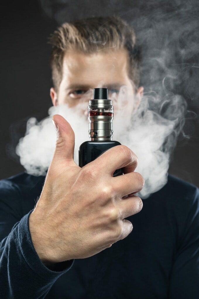 A person holding a genuine vape device with smoke surrounding them, giving a thumbs-up gesture, partially obscuring their face—a perfect snapshot from Vape World GA.