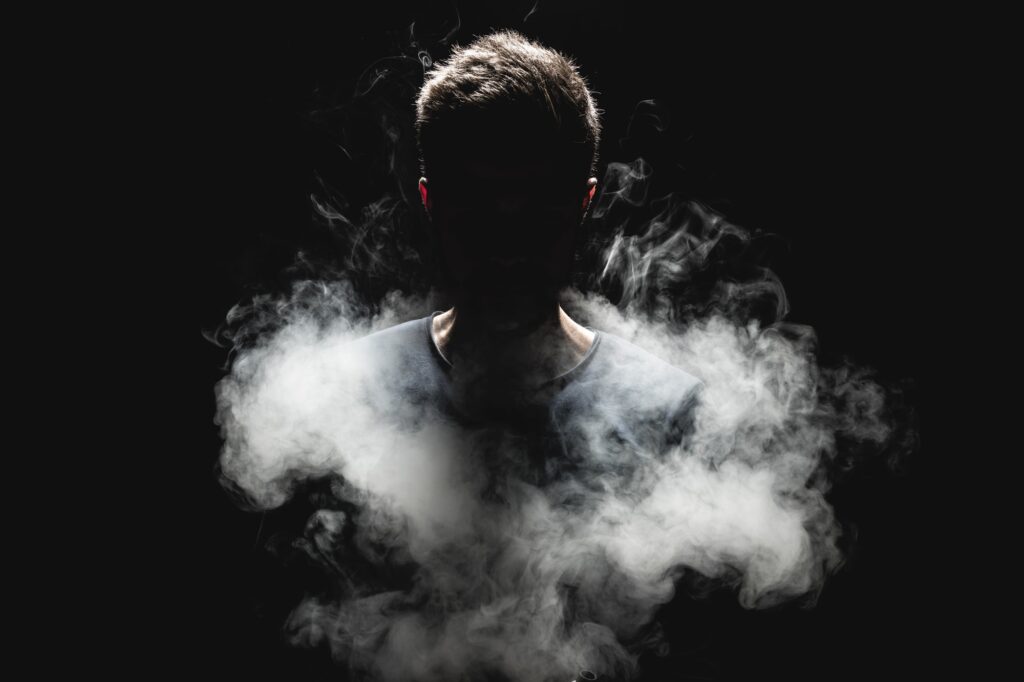 A person standing in a dark environment, partially obscured by swirling smoke.